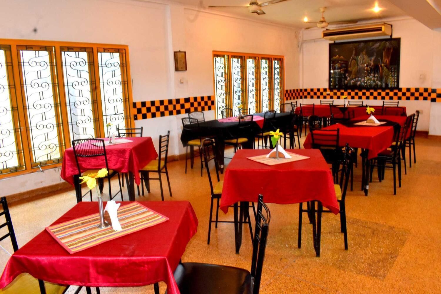 Um restaurante com toalhas de mesa vermelhas, cadeiras pretas e janelas estampadas.