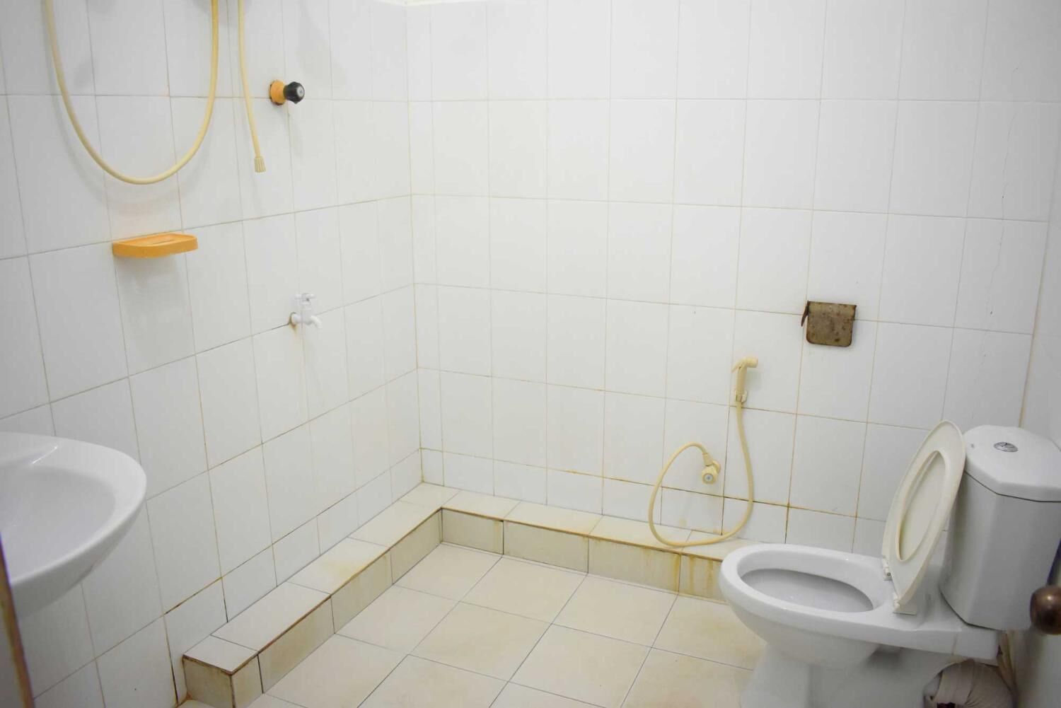 A small, tiled bathroom with a toilet, a sink, and a shower.