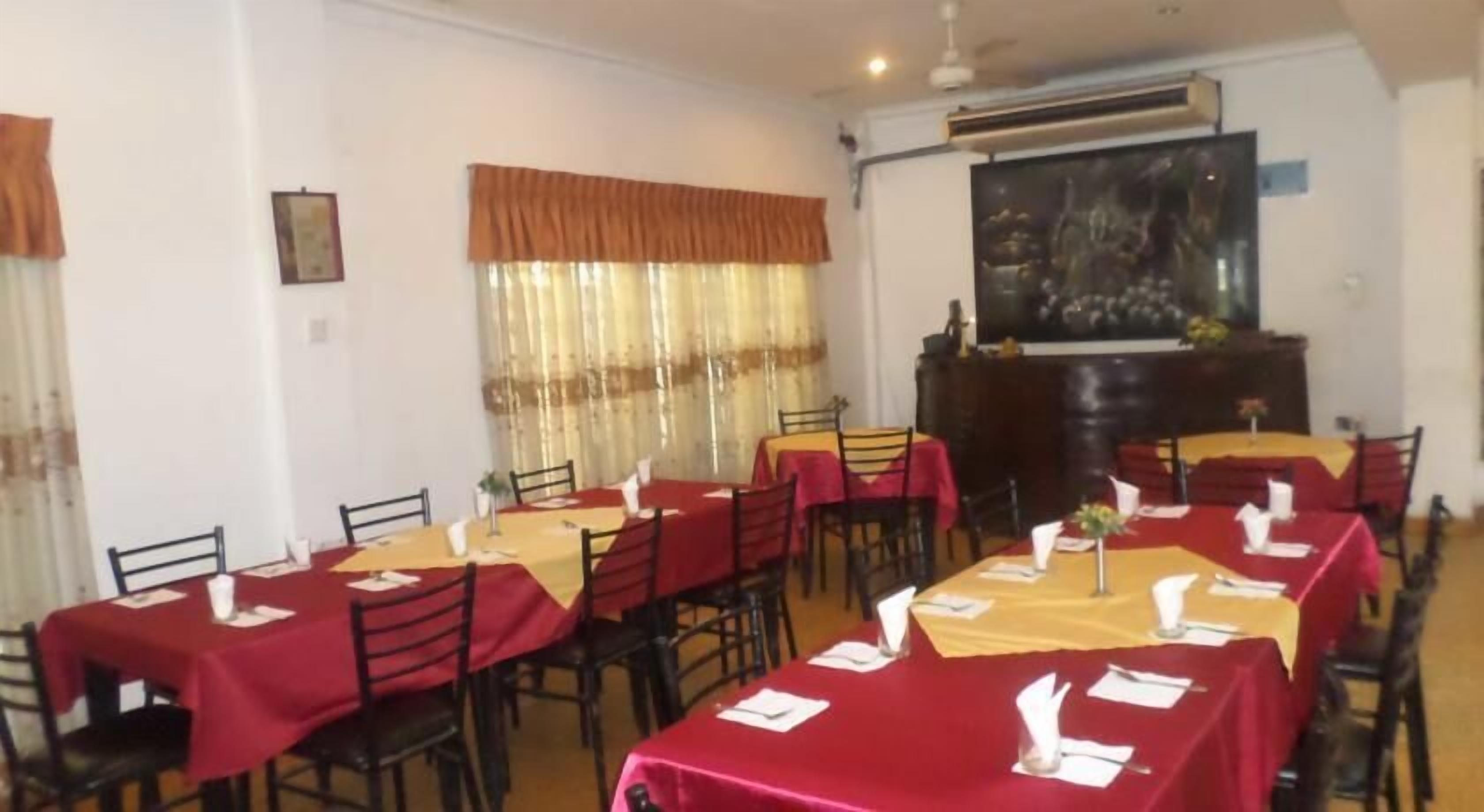 A dining area with tables set for multiple people, featuring red and yellow tablecloths and black chairs.