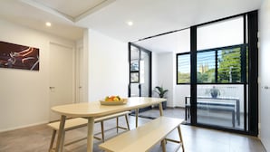 A modern dining area with a wooden table and bench, a bowl of fruit, and a view through a glass door to an outdoor balcony. - Veriu Camperdown (Camperdown)