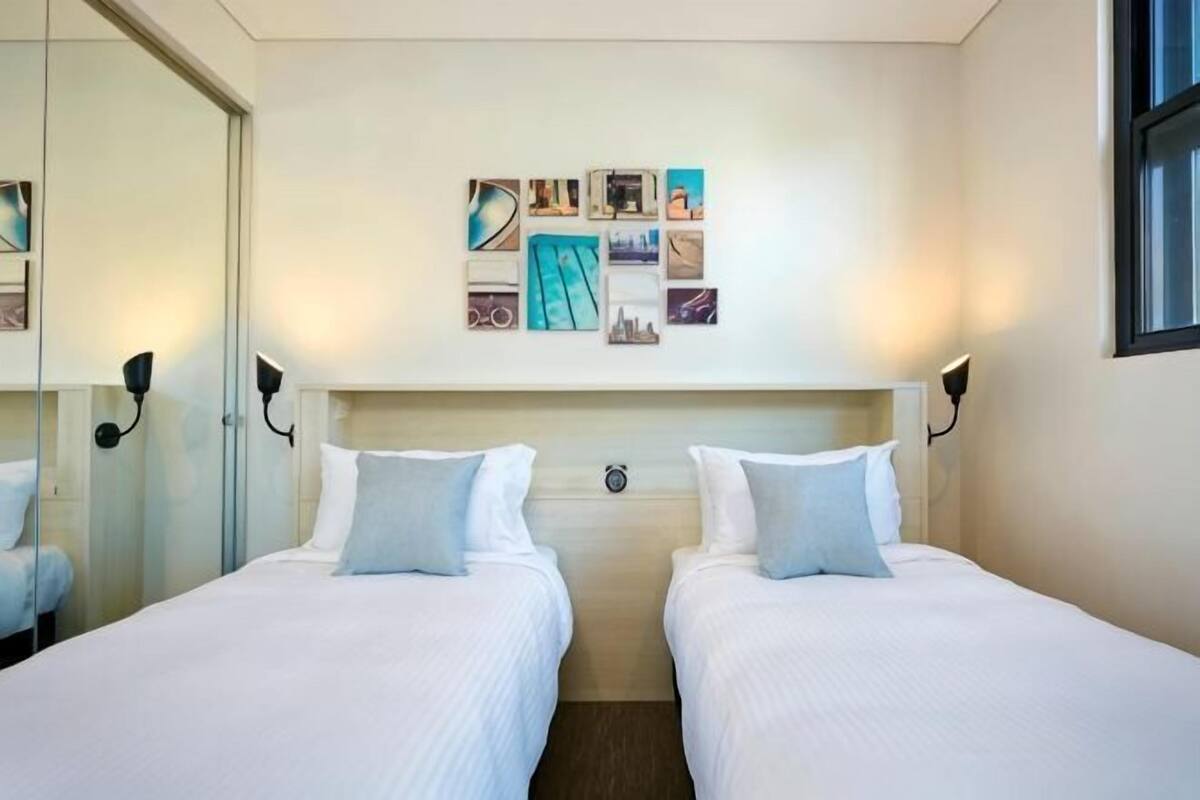 A hotel room with two beds, a headboard with a clock, wall-mounted artwork, and a window.