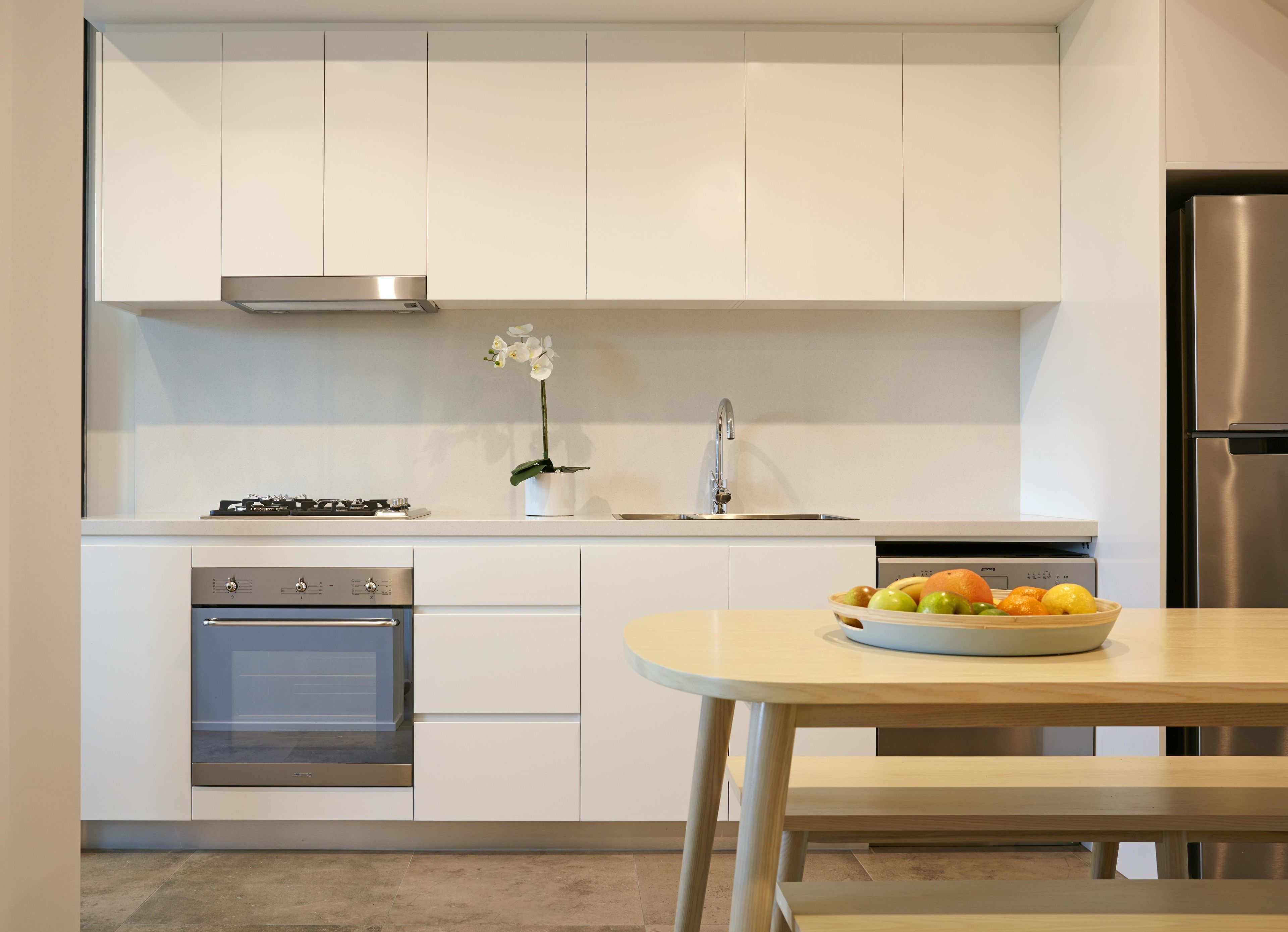 A modern kitchen with white cabinets, stainless steel appliances, a sink, and a bowl of fruit on the counter.