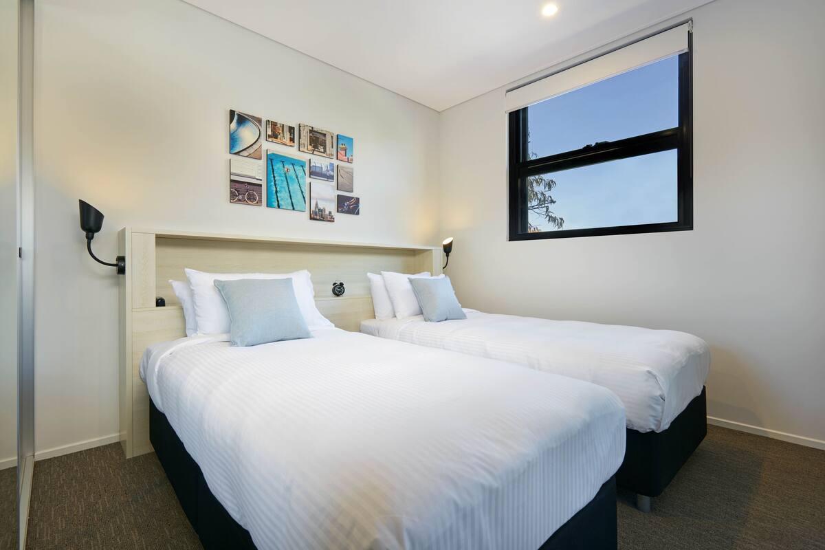 A hotel room with two beds, a large window, and wall art.