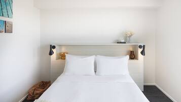 A neatly made bed with white linens, a brown throw blanket, and a small brown bag on the floor.