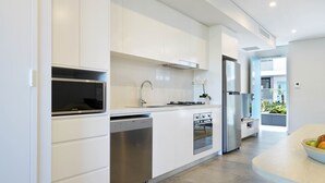 A modern kitchen with white cabinetry, stainless steel appliances, and a bowl of fruit on the counter. - Veriu Camperdown (Camperdown)