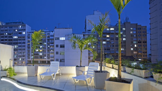 Terraza en la azotea con sillones de descanso, plantas en macetas y vistas de edificios altos circundantes.