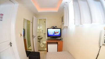 A compact hotel room with a bed, a small desk with a television, a mini-fridge, and a bathroom visible through an open door.