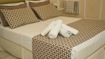 Cama bem arrumada com colcha estampada e almofadas, e toalhas enroladas sobre a cama.