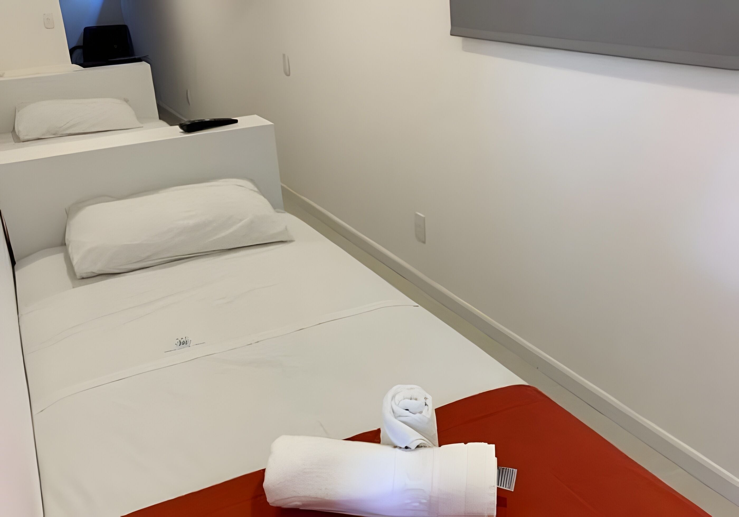 A hotel room with a bed, pillows, a folded towel, and a wall-mounted light switch.