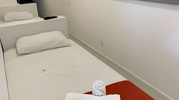 A hotel room with a bed, pillows, a folded towel, and a wall-mounted light switch.