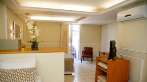 Habitación de hotel con cama, escritorio, silla, televisor y ventana con cortinas.