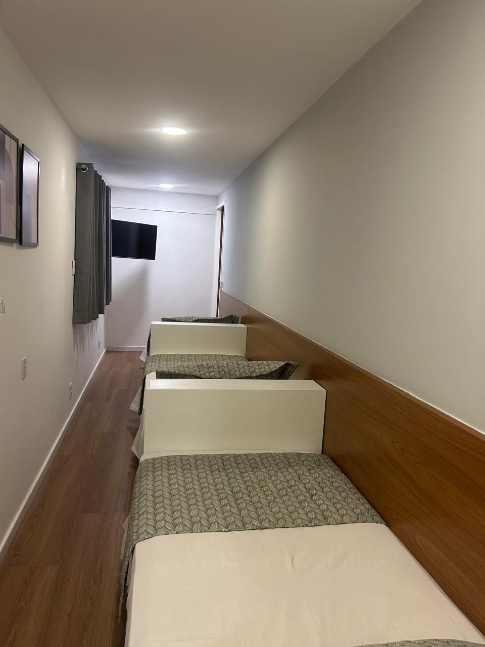 Un pasillo con cuatro camas dispuestas junto a la pared, un televisor de pantalla plana montado en la pared y suelo de madera.