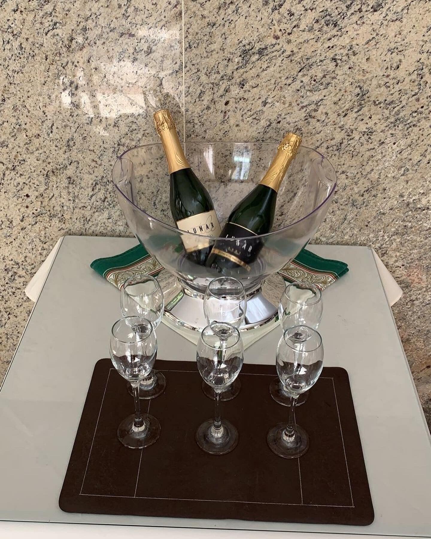 A clear glass bowl with two champagne bottles and three wine glasses on a tray.