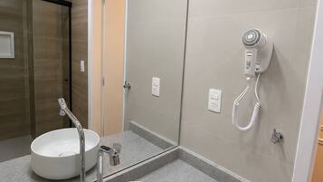 A bathroom with a large mirror, two sinks, a shower area, and a hairdryer mounted on the wall.