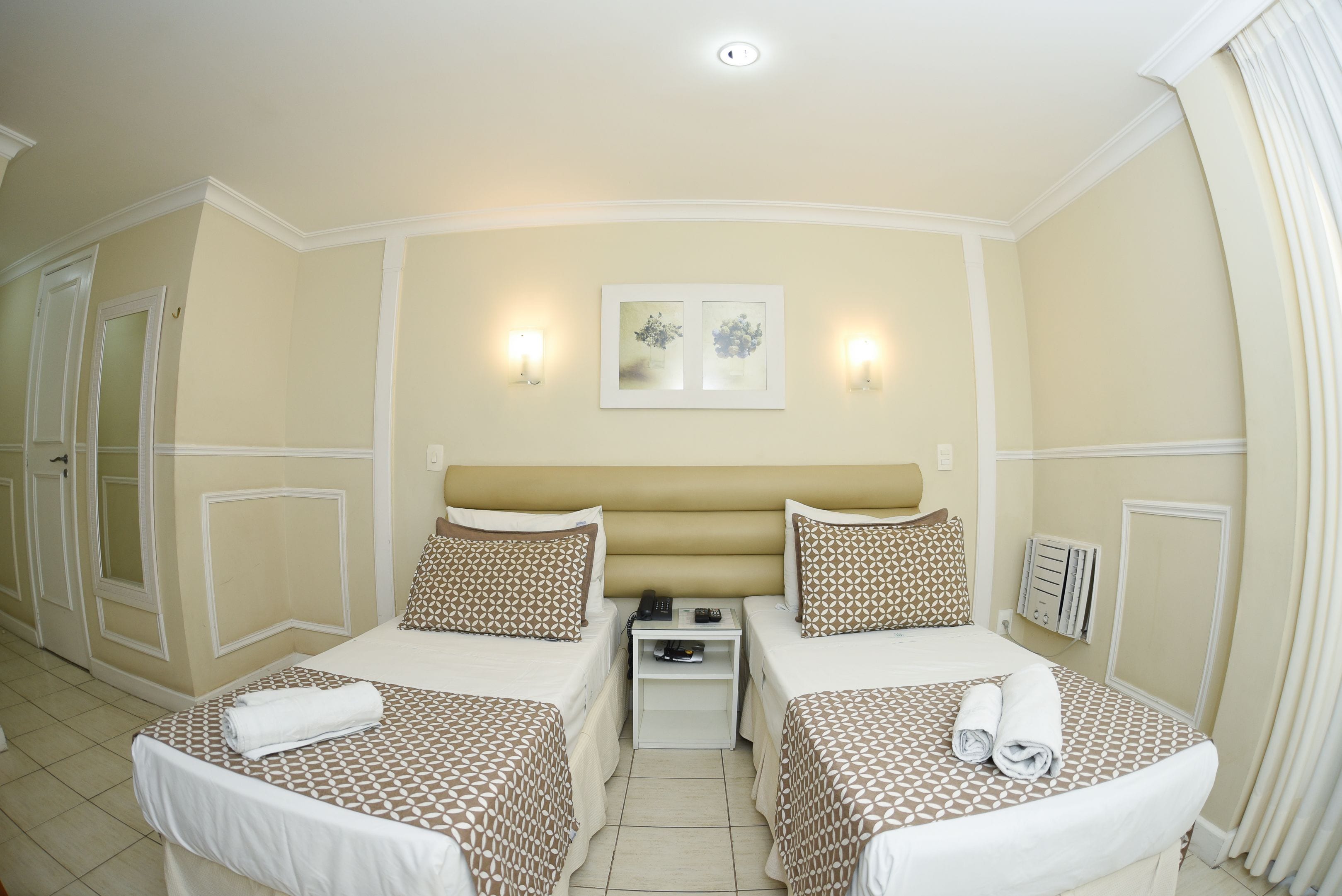 Une chambre d’hôtel avec deux lits, une table de chevet et un luminaire fixé au mur.