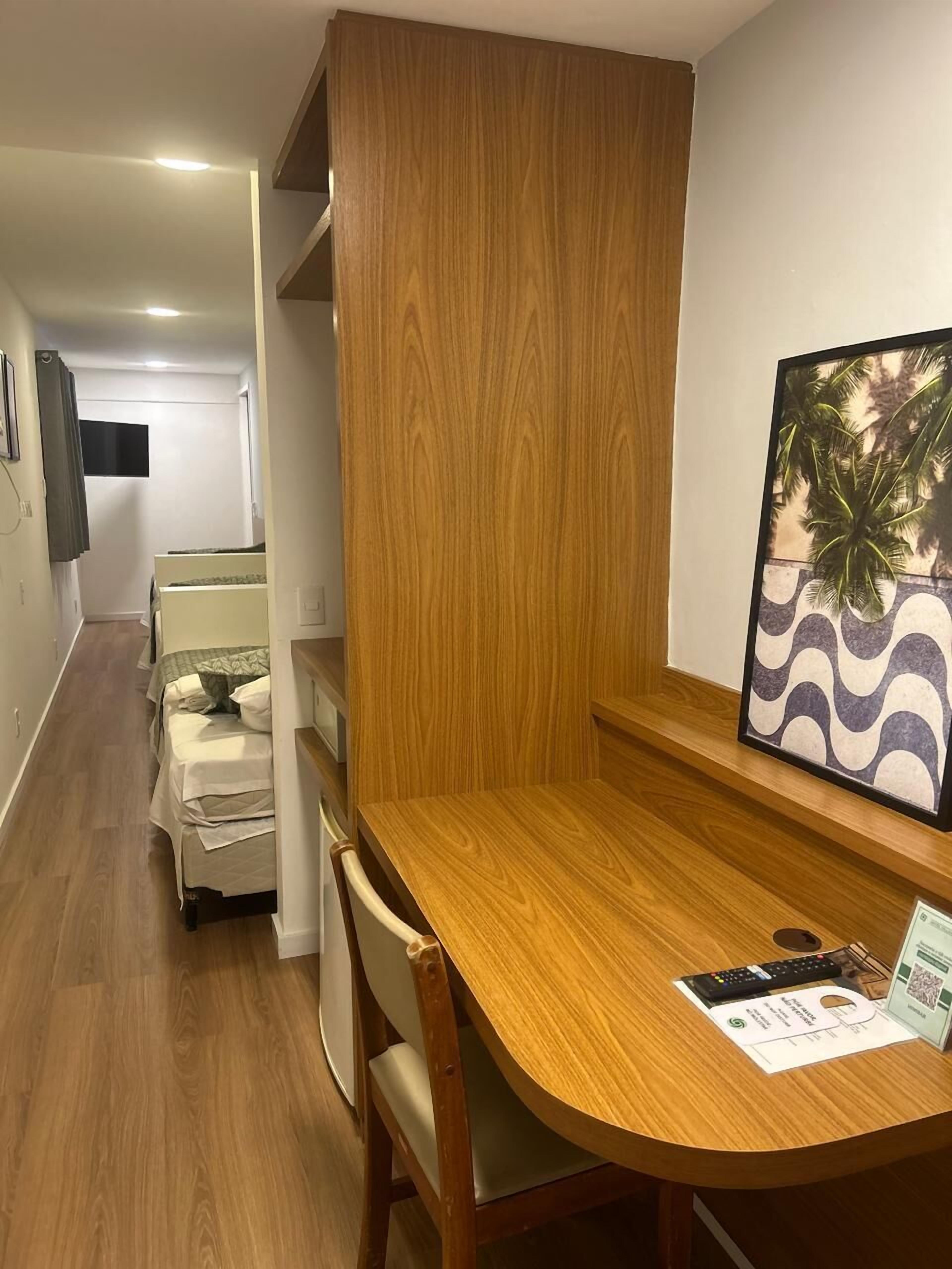 Una mesa de comedor de madera con sillas, un cuadro enmarcado con palmeras y una lámpara de mesa pequeña.