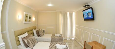 Quarto de hotel com duas camas, uma TV fixada na parede e uma pequena mesa de madeira.
