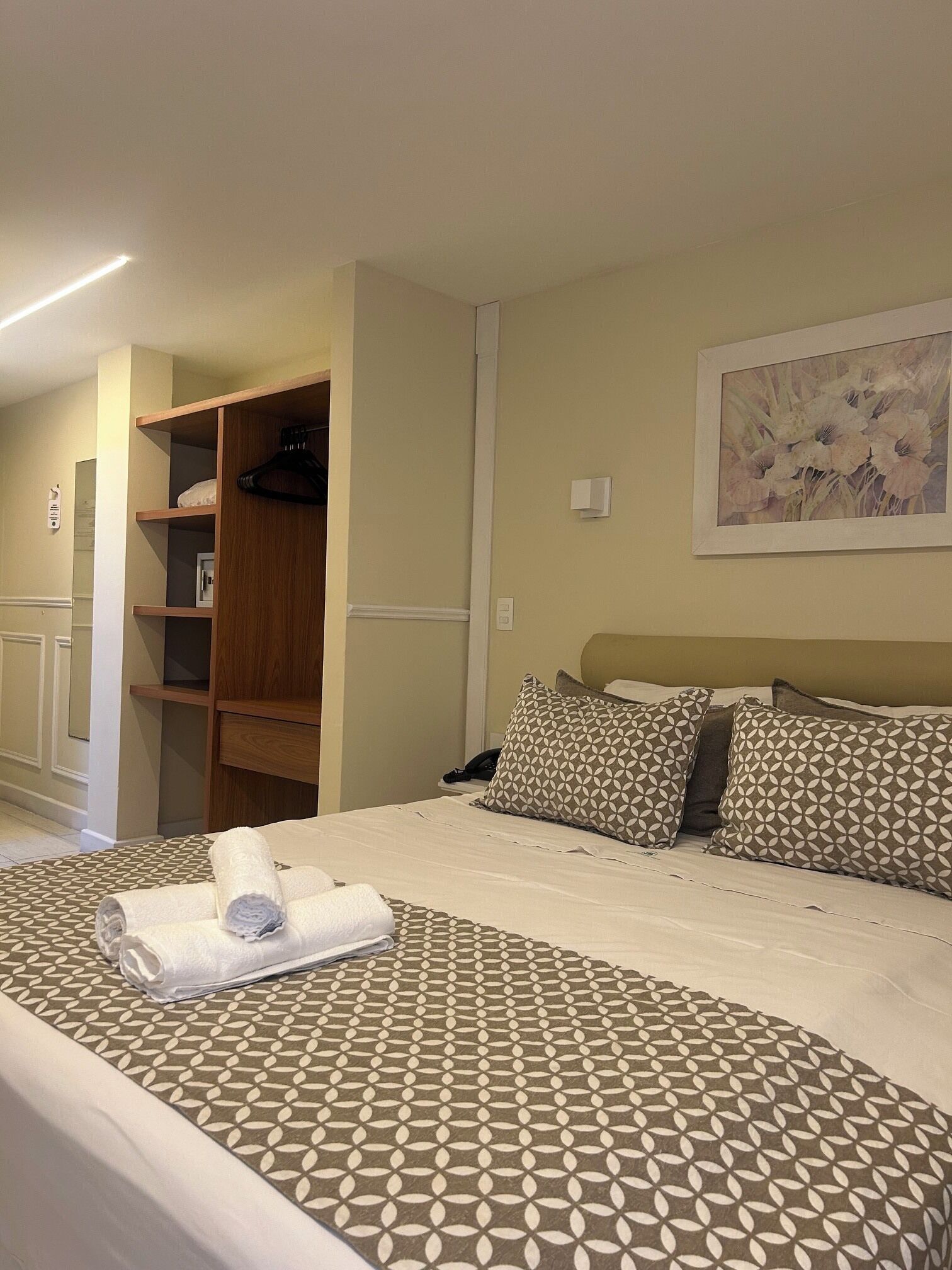 Une chambre d’hôtel avec un lit, une armoire en bois, un tableau au mur et une couvre-lit à motifs.