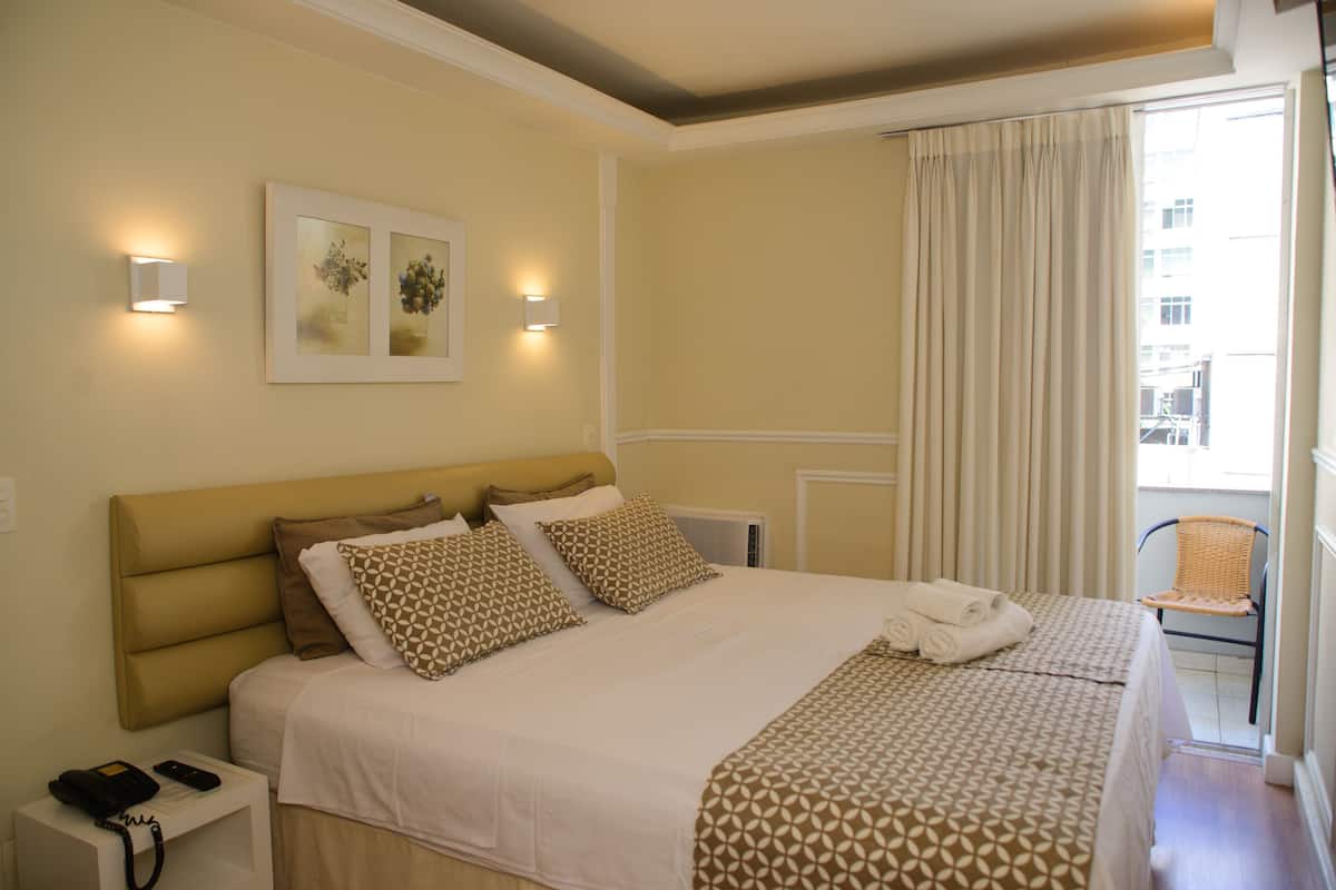 Een hotelkamer met een groot bed, een telefoon op het nachtkastje en een stoel bij het raam.