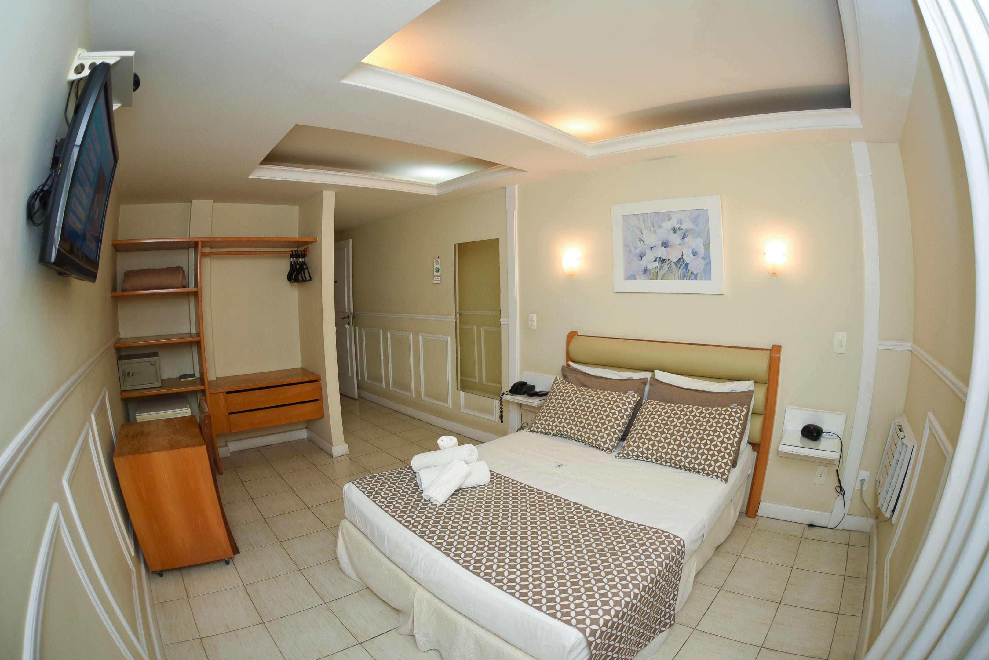 Una habitación de hotel con cama, escritorio, silla, armario y televisor.