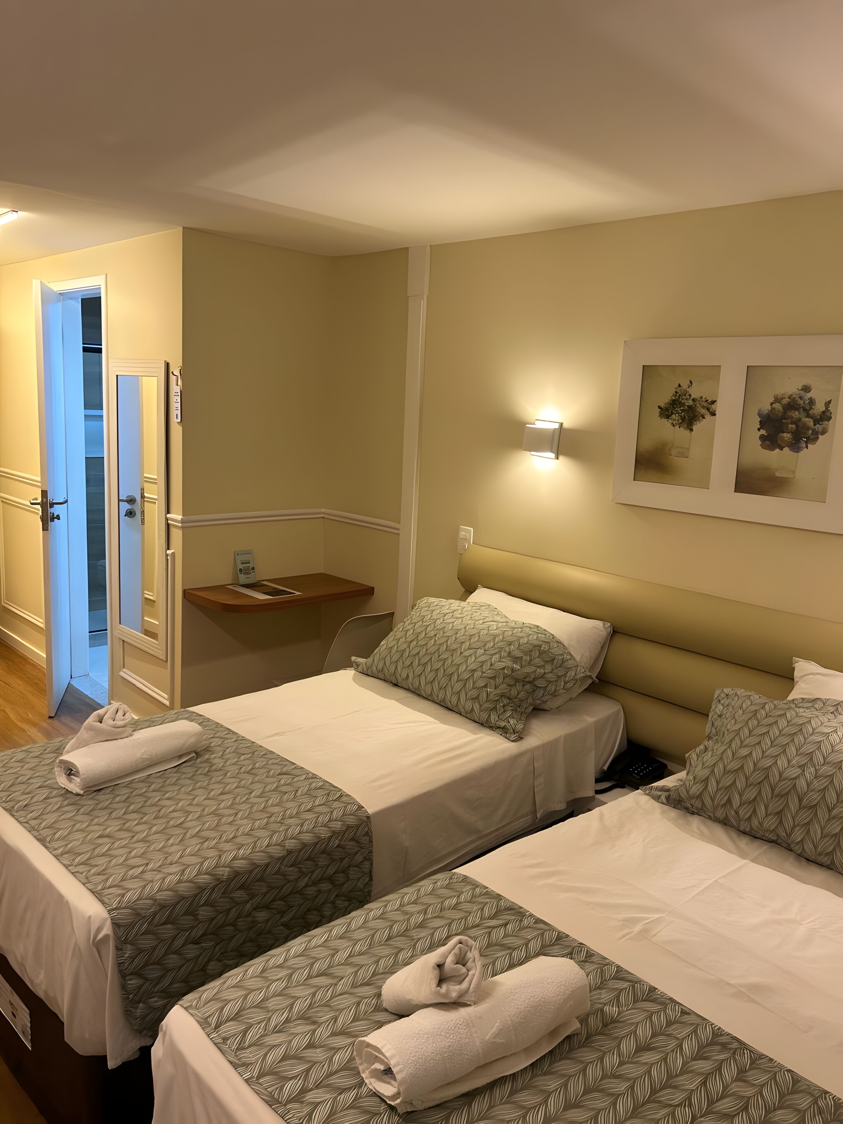 Habitación de hotel con dos camas, una mesita de noche, una lámpara de pared y un cuadro enmarcado.