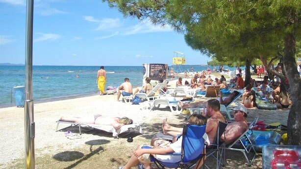 A beach scene with people relaxing on sun loungers and chairs, a lifeguard tower, and a clear view of the sea. - Apartments Ljiljana (Zadar)