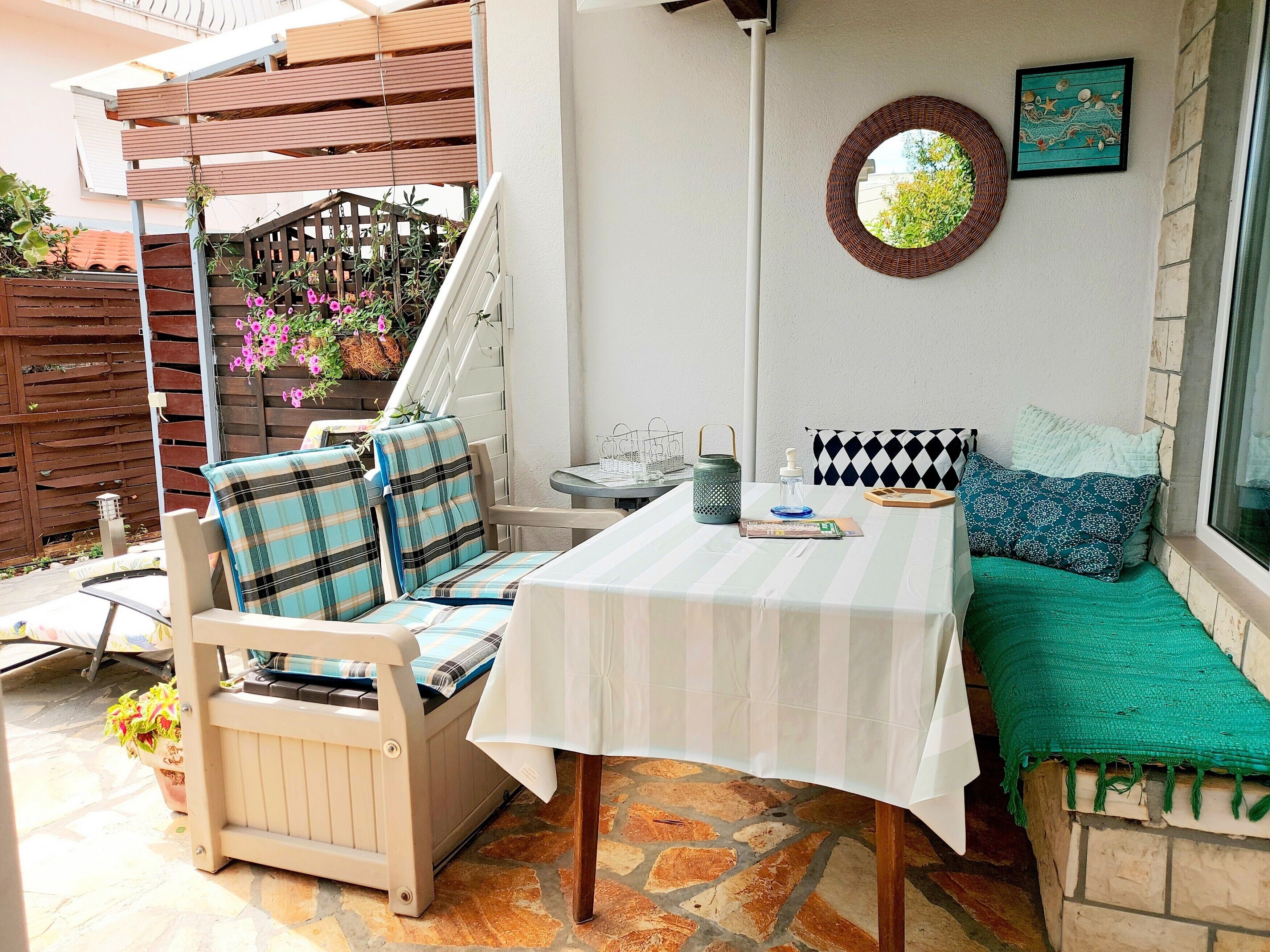 A patio with a table and chairs, a bench, a hanging basket with flowers, and a wall-mounted mirror.