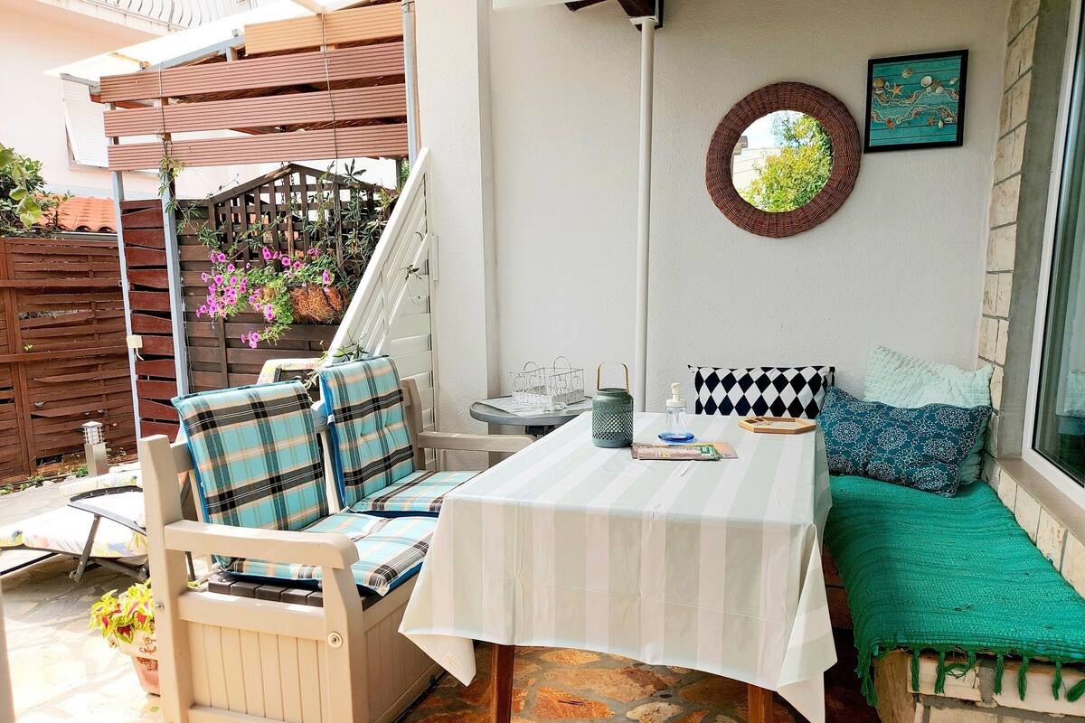A patio with a table and chairs, a bench, a hanging basket with flowers, and a wall-mounted mirror.