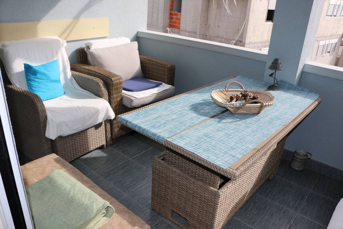 A balcony with wicker furniture, a table with a blue mat, and a small lamp.