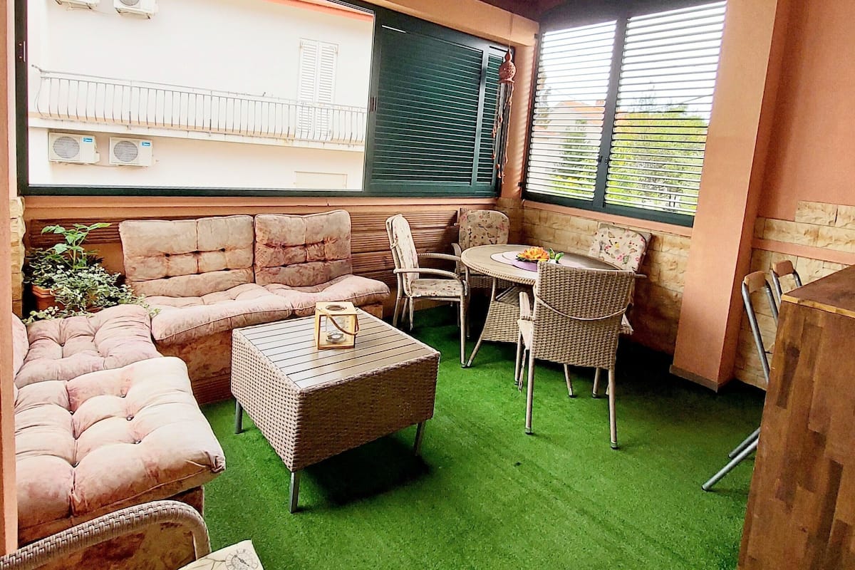 A cozy patio area with a cushioned sofa, wicker chairs, and a small table.