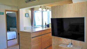 A modern hotel room with a wooden floor, a large flat-screen TV mounted on a wooden panel, a small desk with a chair, and a window with curtains. - Apartments Ljiljana (Zadar)