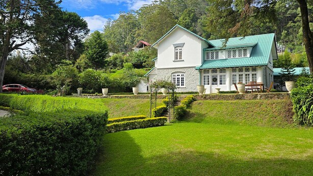 Een wit huis met een groen dak, omgeven door weelderige begroeiing en bomen.