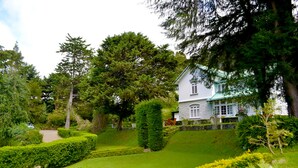 Een wit huis met een groen dak, omgeven door weelderige begroeiing en een verzorgde tuin.