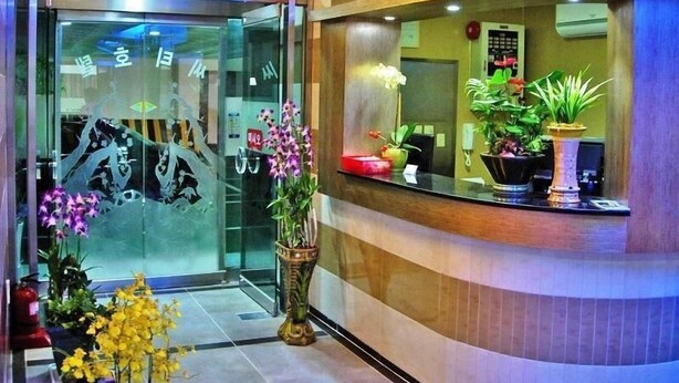 Un área de recepción con puerta de vidrio, plantas en macetas y un mostrador curvo.