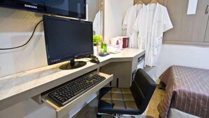 Habitación de hotel con una televisión Samsung, un escritorio con computadora, una silla, una cama y un armario con ropa colgada.