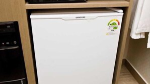 Un refrigerador Samsung con un adhesivo, un microondas y un electrodoméstico negro sobre un estante de madera.