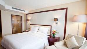 Quarto de hotel com uma cama grande, mesa de cabeceira com abajur, sofá e chuveiro.