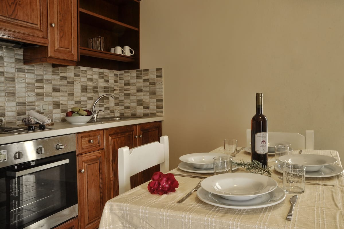 A kitchen with a tiled backsplash, wooden cabinets, a built-in oven, and a dining table set with plates, glasses, and a bottle.