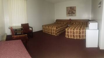 A hotel room with two beds, a small table with a chair, a refrigerator, and a painting on the wall.