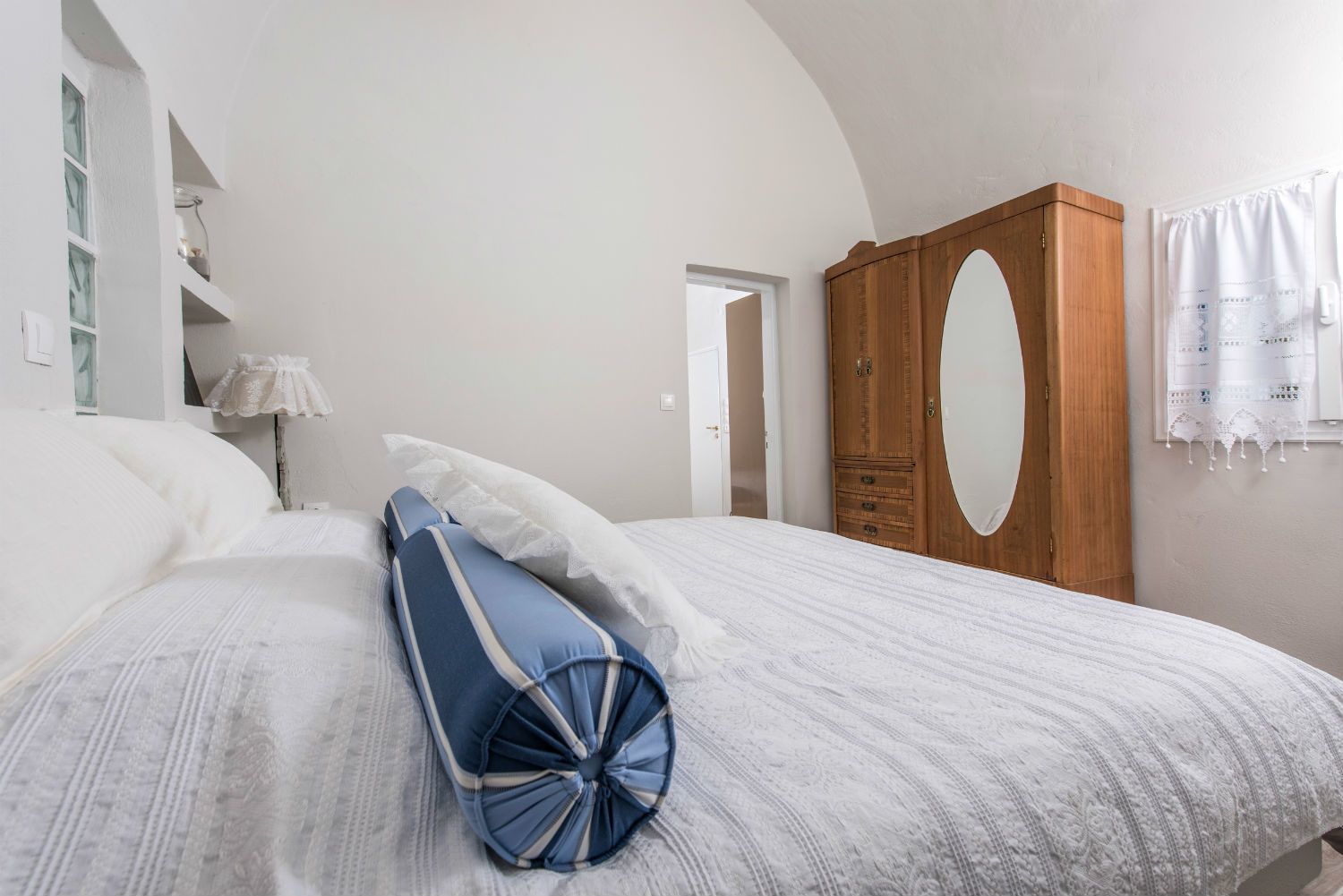 Ein Schlafzimmer mit einem Bett, einem Holzschrank, einem Spiegel und einem Fenster mit Vorhängen.