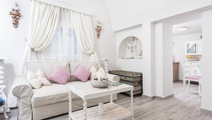 A cozy living room with a sofa, a coffee table, and a decorative mirror. - Villa Iokasti (Santorini)