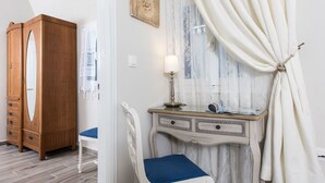 A room with a wooden wardrobe, a desk with a lamp, a chair, and a window with curtains. - Villa Iokasti (Santorini)