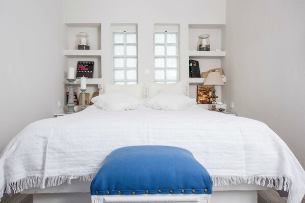 A neatly arranged bedroom with a large bed, two windows, and shelves with decorative items.