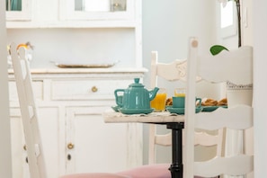 A breakfast setup with a teal teapot, cups, and orange juice on a white table.