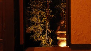 A doorway with a bamboo plant inside, a wooden bench to the left, and a textured wall.