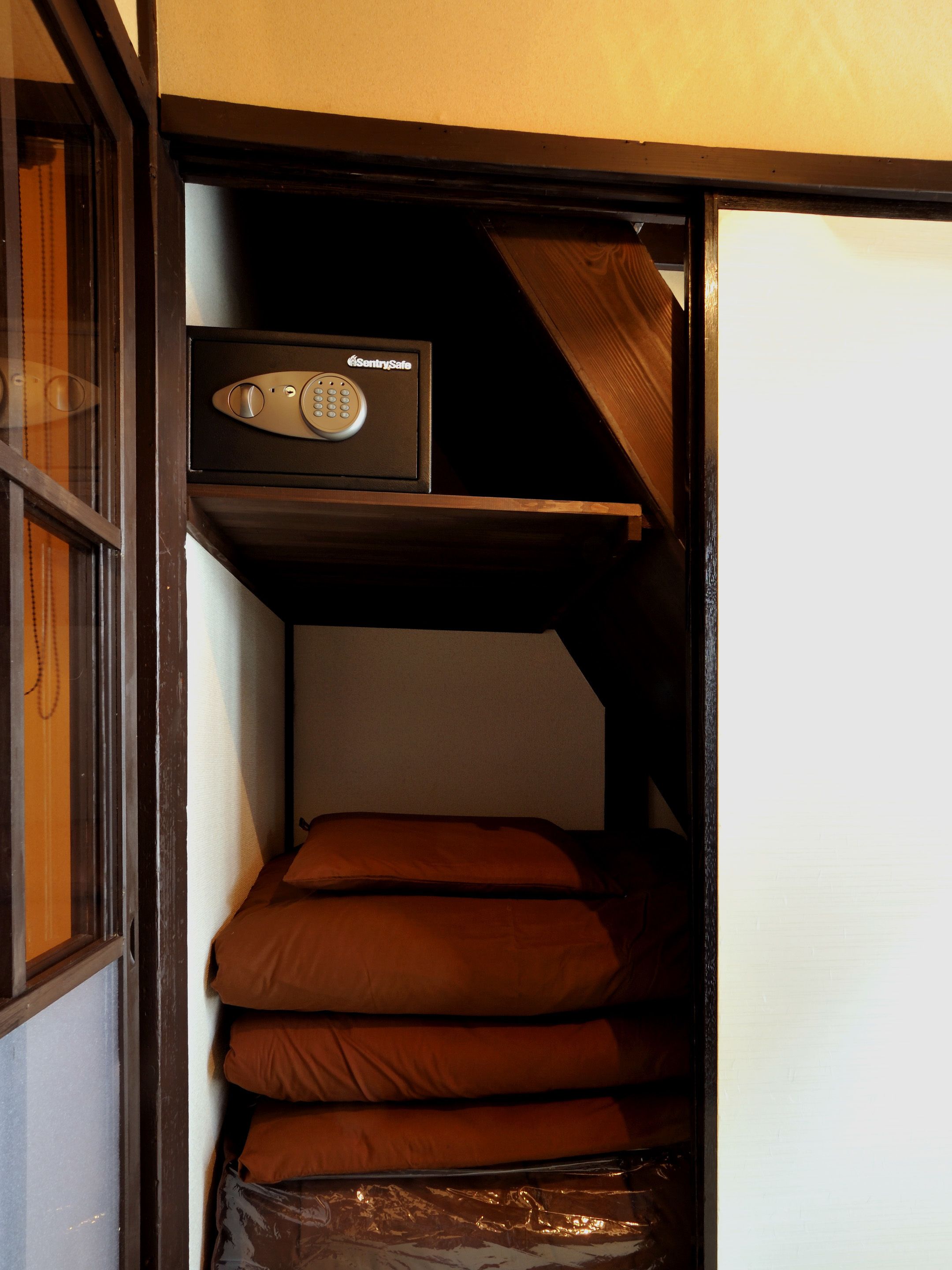 A compact room with a bunk bed, a small shelf with a safe, and a window with blinds.