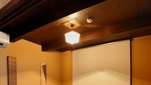 A traditional Japanese-style room with tatami flooring, a television, a projector screen, and a wooden table with a remote control.