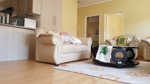 Ein Wohnzimmer mit einem beigefarbenen Sofa, einem Couchtisch mit einer Zimmerpflanze und einem gemusterten Teppich.