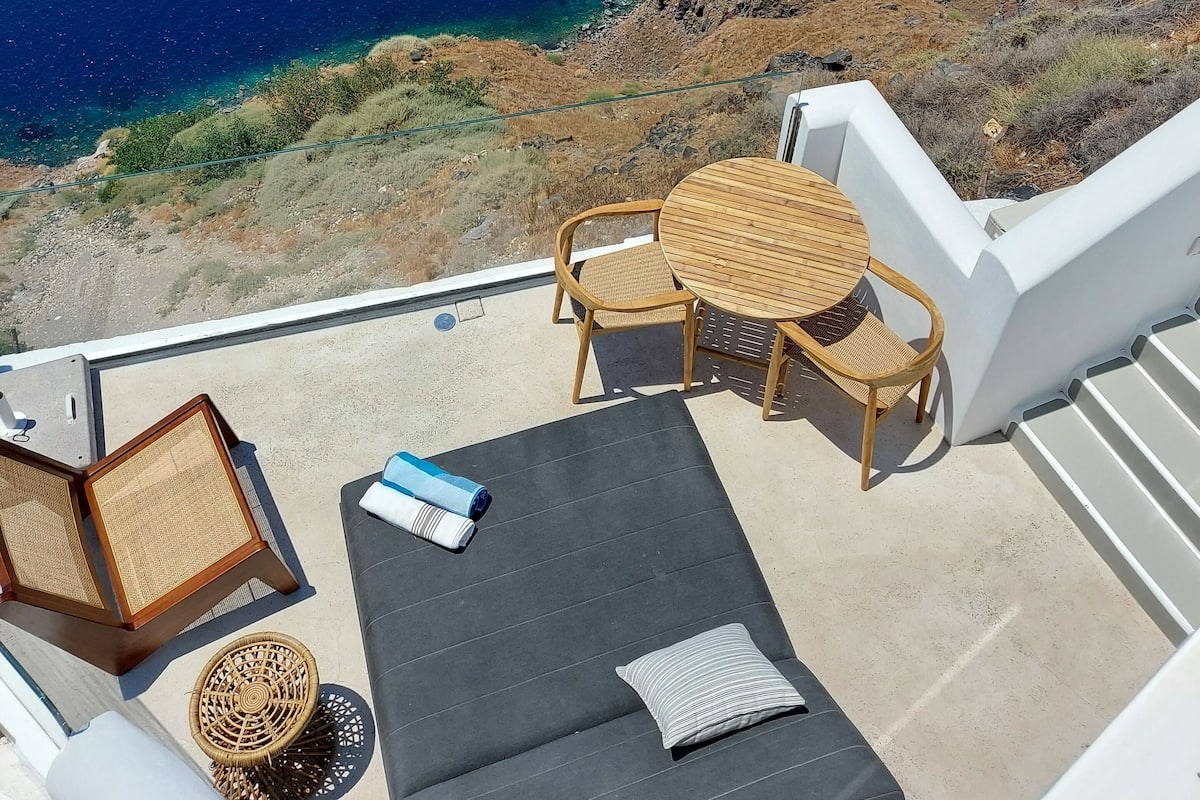 Un balcón con vista al mar, una mesa redonda con sillas, un sofá y una pequeña mesa con una silla.