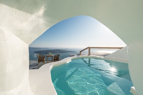 Ein Infinity-Pool mit Blick auf das Meer, ein Holztisch mit Stühlen und ein klarer Himmel.